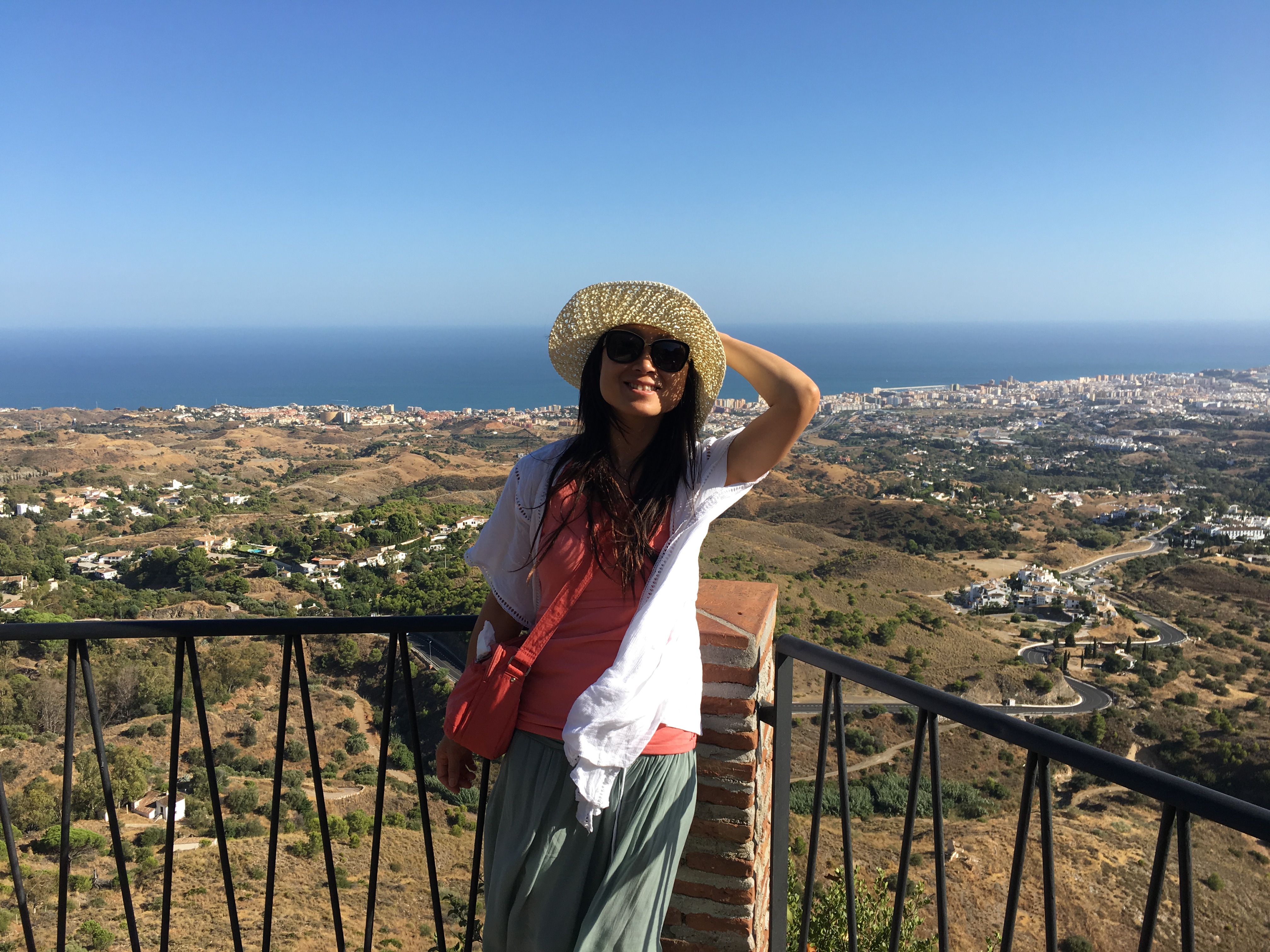 Connie in a sun hat at a mountain viewpoint, soft coastline and hills below