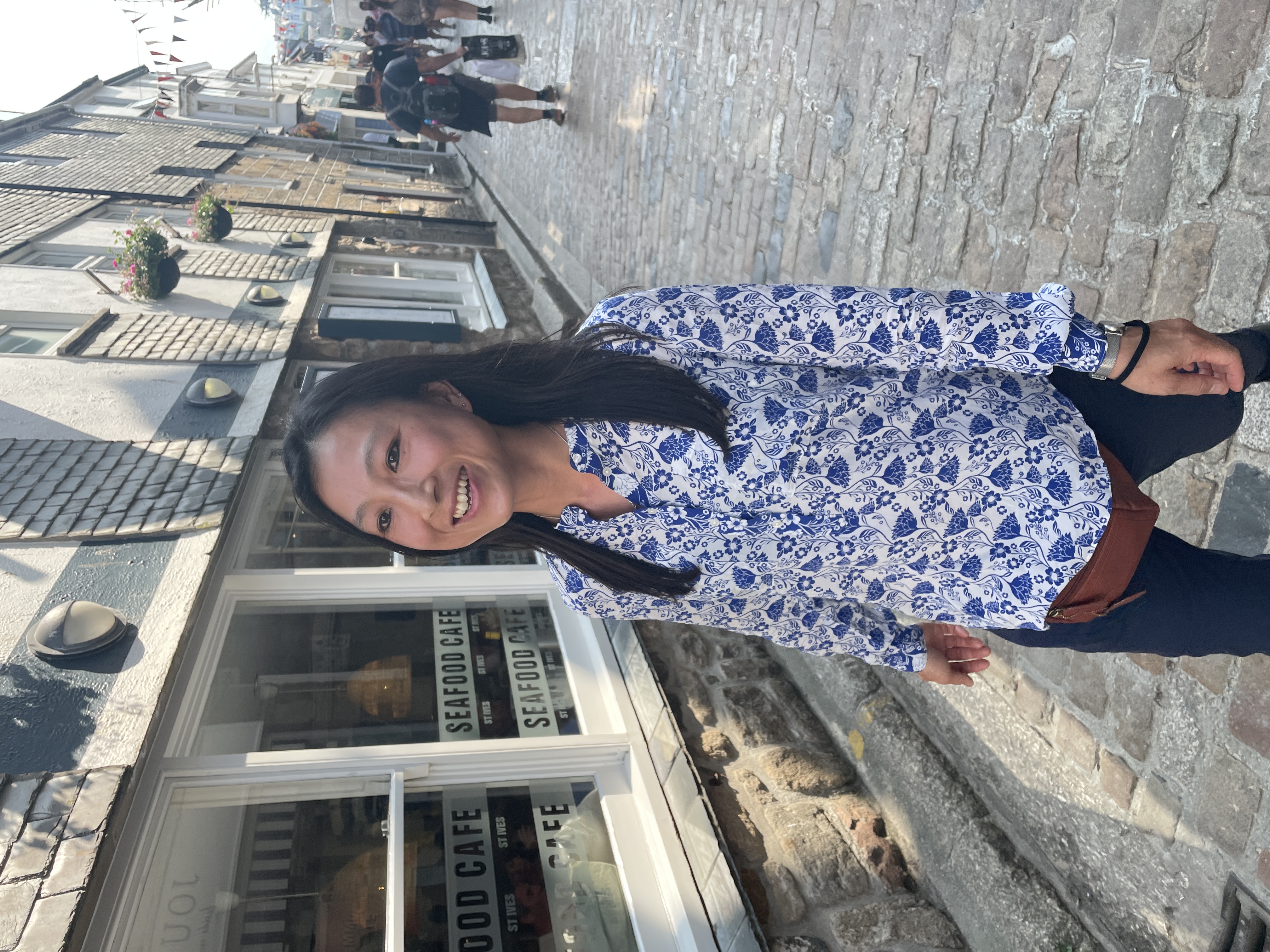Connie smiling on a Hong Kong street, a SEAFOOD CAFE sign behind her, cobblestones underfoot